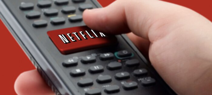 A hand pressing a Netflix button on a remote control.