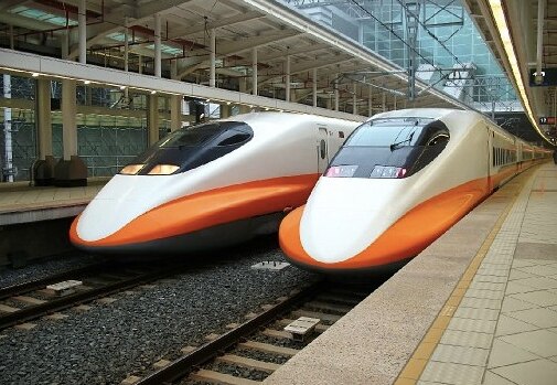 Two high-speed trains with orange and white designs parked at a modern train station.