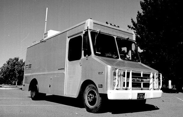 A vintage food truck in black and white,parked in a lot with trees in the background.