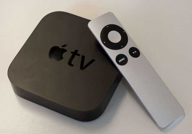 An Apple TV device alongside its remote control on a flat surface.