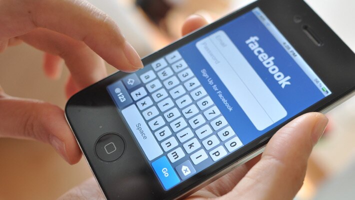 A person using a smartphone displaying the Facebook login screen with a keyboard shown.