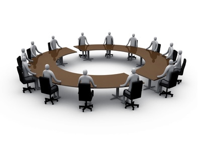 A 3D illustration of a round table meeting with several stylized figures sitting around it.