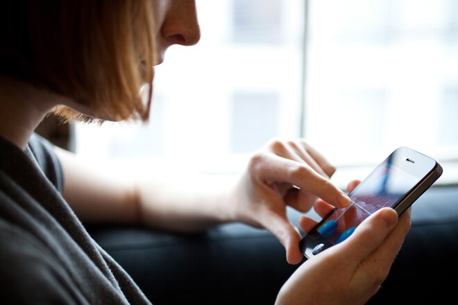 A close-up view of a person using a smartphone while sitting near a window.