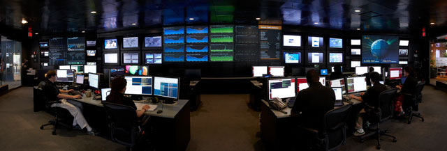 A panoramic view of a high-tech control room filled with multiple screens and monitors displaying data and graphics