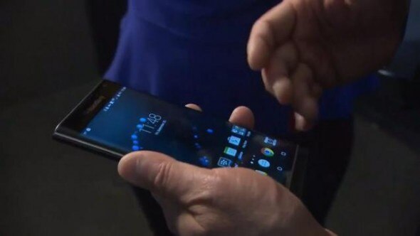 A close-up view of a hand holding a smartphone displaying its home screen.