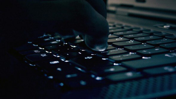 A close-up image showing a hand pressing a key on a dark-lit laptop keyboard.