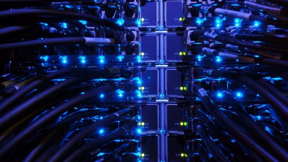 A close-up view of a network server room with numerous cables and blue lights illuminating the equipment.