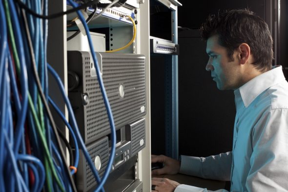 A technician working on a computer server in a server room,surrounded by network cables.