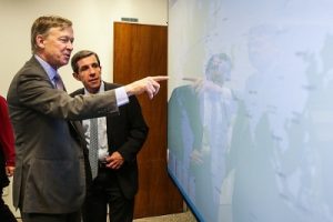 Two men engaged in conversation while pointing at a digital map on a screen in a meeting room.