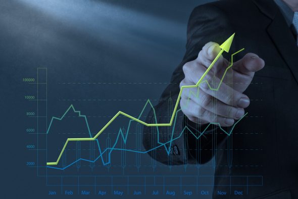 A business professional pointing at an upward-trending line graph with multiple data points.