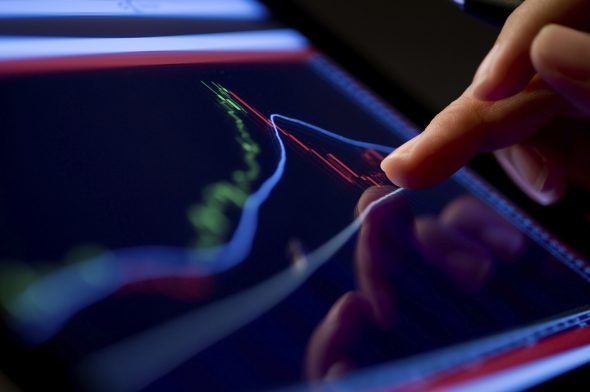 Close-up of a finger touching a financial chart on a touchscreen device.