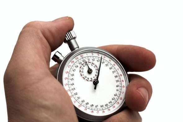 A close-up of a hand holding a silver stopwatch with a white face and red markings.