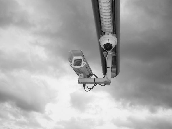 Two security cameras mounted on a pole under a cloudy sky.