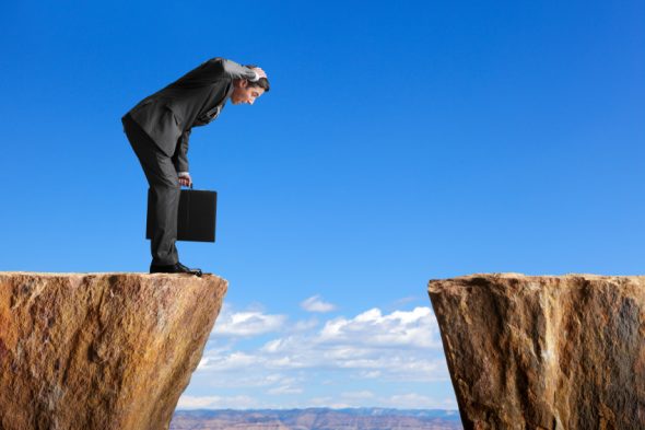 A businessman in a suit looks down from a cliff edge with a briefcase.