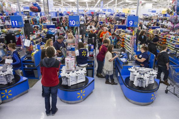 A busy Walmart store checkout area with customers in line and employees assisting shoppers.