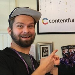 A person with a beard and baseball cap enthusiastically pointing at a Contentful logo on a wall.