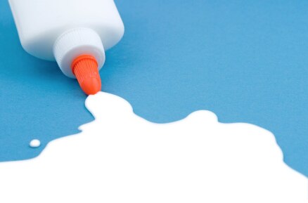 A bottle of white glue with an orange nozzle spilling onto a blue surface.