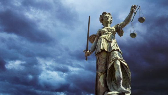 A statue of Lady Justice holding a sword and scales,set against a dramatic cloudy sky.