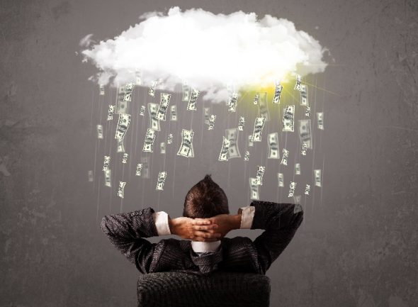 A person in a suit sitting back in a chair with hands behind their head,looking at a cloud raining down dollar bills.