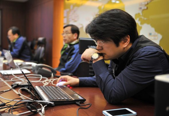 A group of individuals working at a conference table with laptops and phones,focused on their tasks.