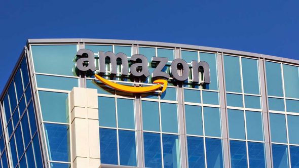 Amazon logo on the side of a modern glass building against a clear blue sky.