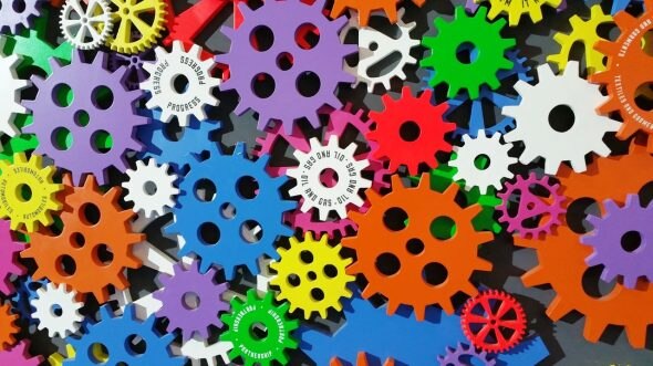 A vibrant arrangement of variously colored gears in purple,green,yellow,orange,blue,and white,set against a dark background.