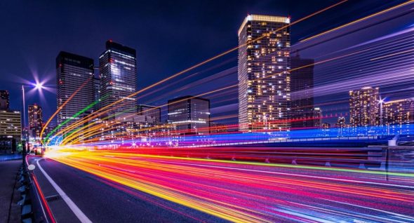 A vibrant cityscape at night with colorful light trails from moving vehicles,showcasing tall buildings illuminated by lights.