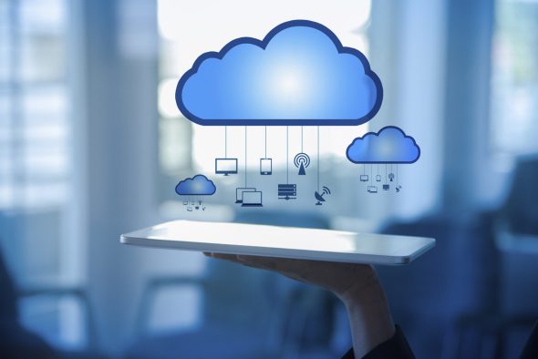 A hand holding a tablet displaying cloud computing icons above,representing various devices connected to the cloud.