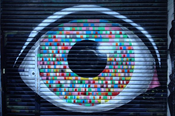 A vibrant mural of an eye painted on a closed metal shutter,featuring various colorful pixels in the iris area.