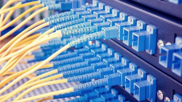 Close-up of fiber optic cables with blue connectors and yellow wires organized on a patch panel.