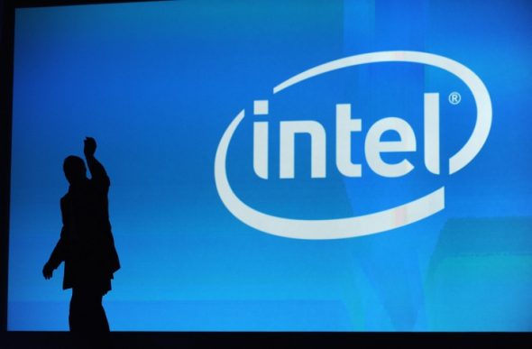 A silhouette of a person gesturing in front of a large blue screen displaying the Intel logo.