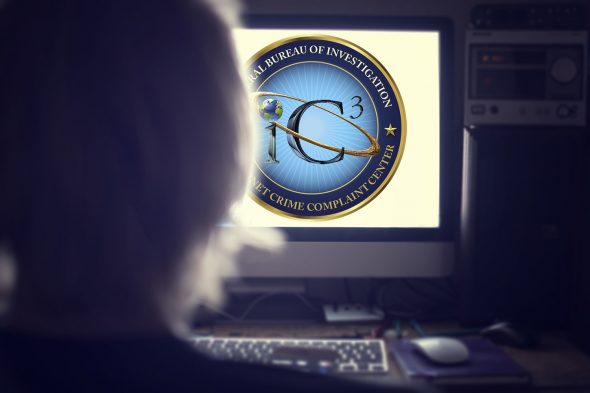 A person sitting in front of a computer screen displaying the logo of the FBI's Internet Crime Complaint Center (IC3).