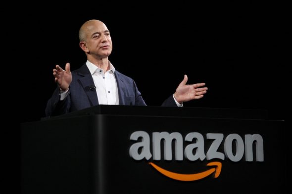 A man speaking at a podium with the Amazon logo,gesturing with his hands.