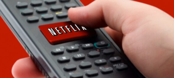 A hand pressing the Netflix button on a remote control with a red background.