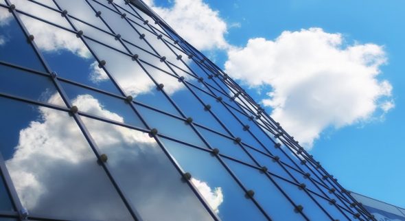 Close-up view of a modern building facade with reflective glass panels and a blue sky with clouds.