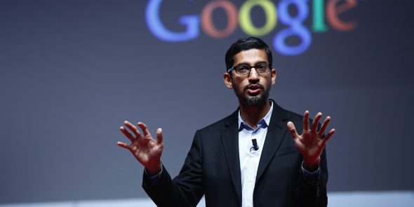 A person presenting on stage with their hands raised,in front of a backdrop displaying the Google logo.