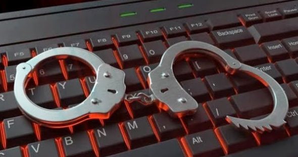 A pair of metallic handcuffs resting on a computer keyboard with glowing red keys.