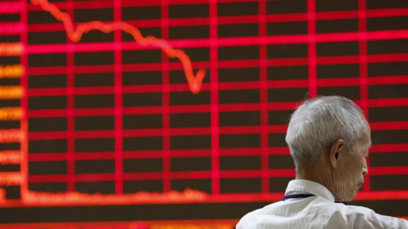 An elderly man looking at a stock market chart displaying a significant downward trend with red indicators.