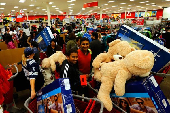 A busy store during a Black Friday sale with shoppers filling their carts with large teddy bears and electronics.