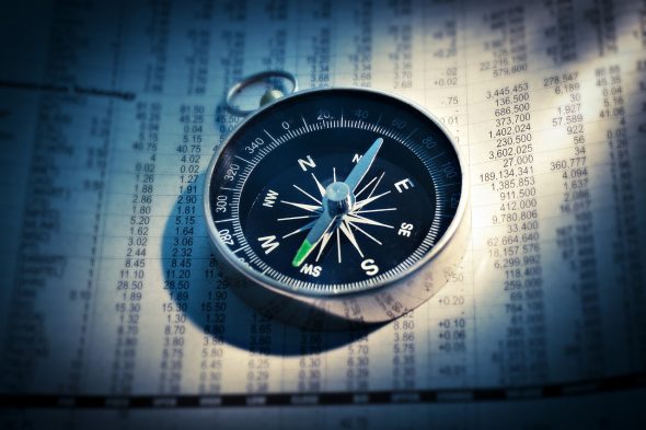 A compass resting on a sheet of financial data or printed numbers.