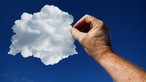 A hand holding a fluffy white cloud against a clear blue sky.