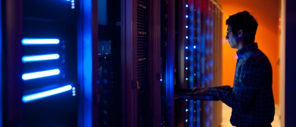 A person interacting with servers in a dimly lit server room,illuminated by blue LED lights.