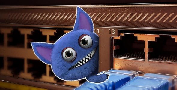 A cartoonish blue monster with large eyes and a wide grin peeking out from behind network ports.