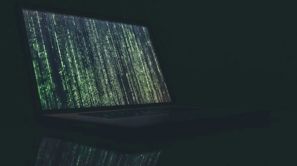 A laptop displaying green matrix code against a dark background.