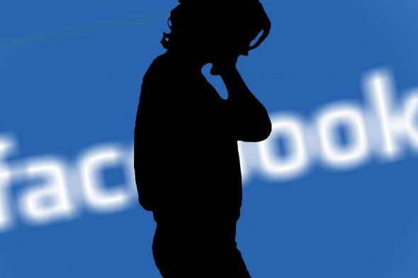 A silhouette of a person with their head down against a blurred Facebook logo background.