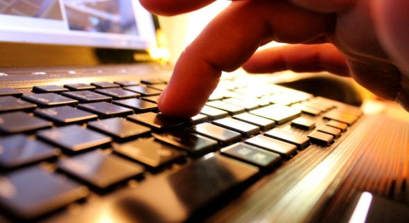 A close-up view of a hand pressing a key on a laptop keyboard.