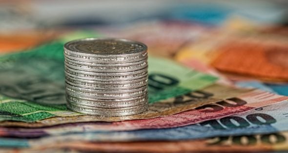 A stack of coins placed on a variety of colorful banknotes arranged beneath.