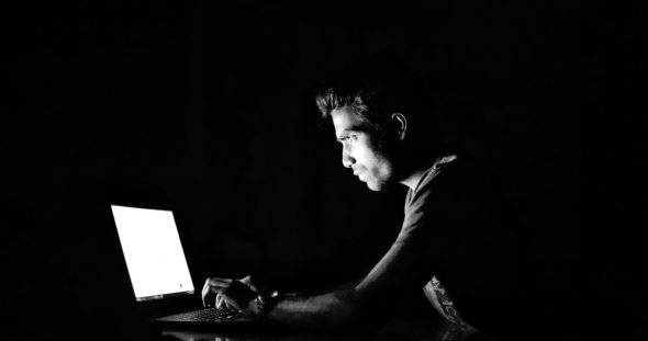 A person focused on a laptop screen in a dark environment,illuminated by the screen's light.