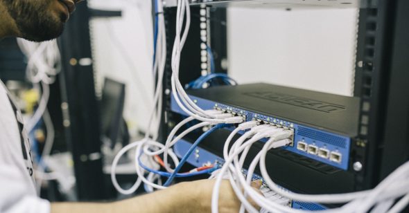 A technician working on a network rack,managing multiple cables connected to networking equipment.