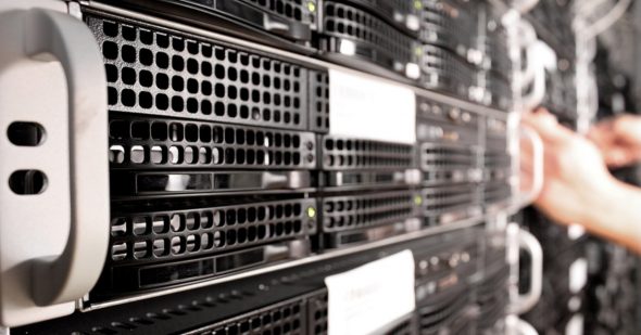 Close-up view of a server rack with black servers and a person's hands working on it.